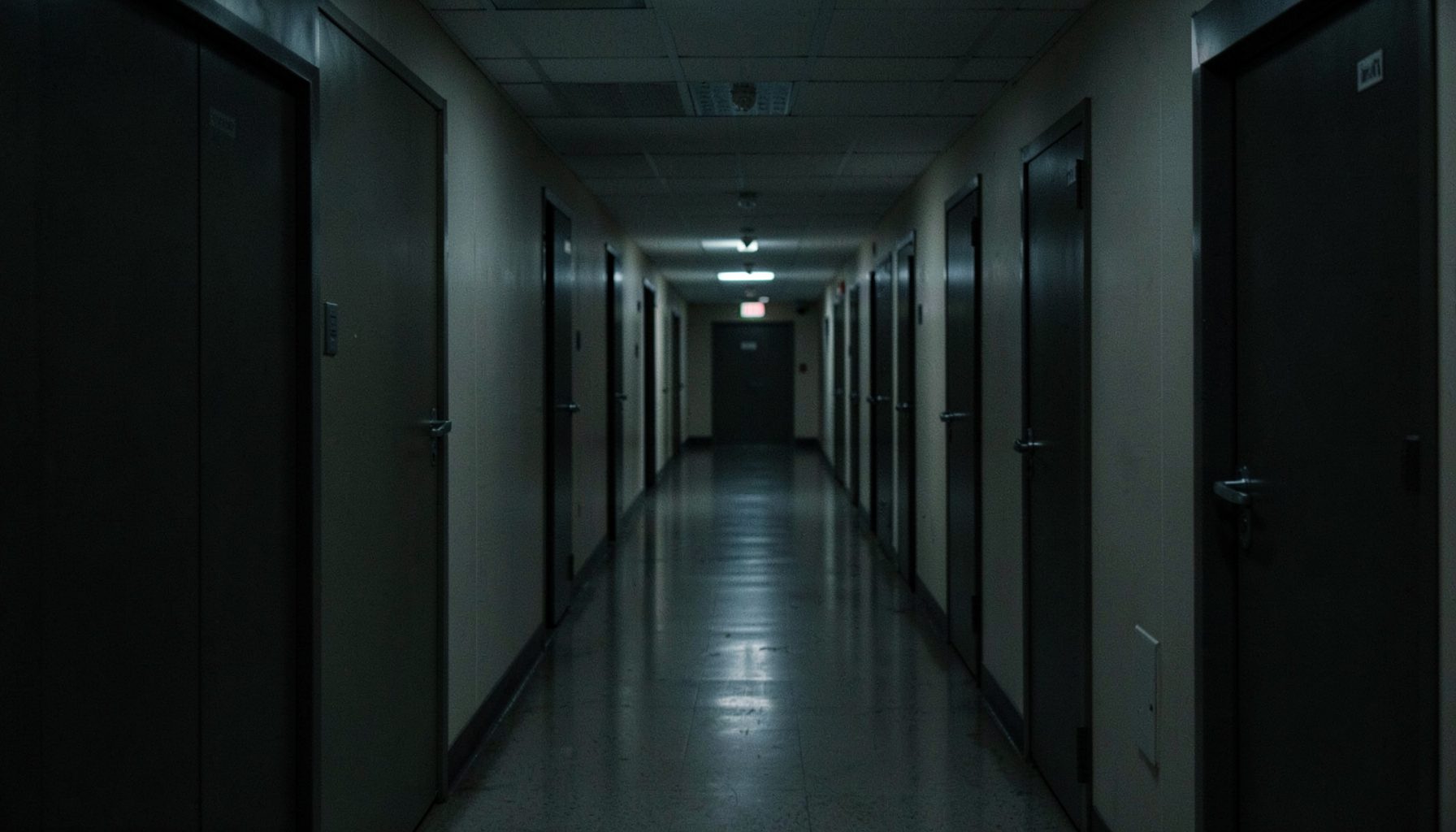 A dimly lit institutional hallway with rows of closed doors, conveying a sense of opaque decision-making and distant bureaucratic power